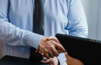 Business handshake between colleagues in a formal office meeting setting.