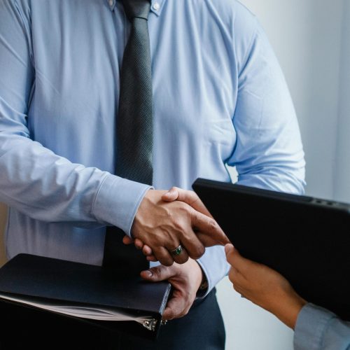 Business handshake between colleagues in a formal office meeting setting.